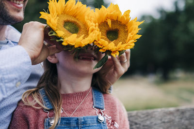 Man covering girl's face with sunflowers at park