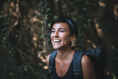 Portrait of smiling young woman standing in forest with a backpack