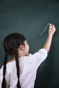 Rear view of girl writing on blackboard