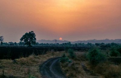 Road amidst trees against sky during sunset