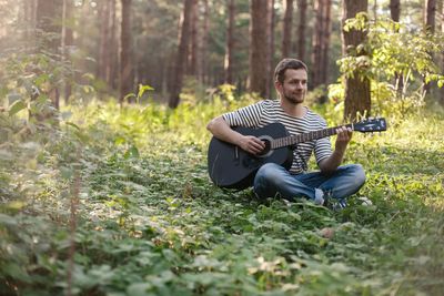 Young man sitting on tree in forest