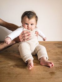 Portrait of cute baby girl sitting on table against wall