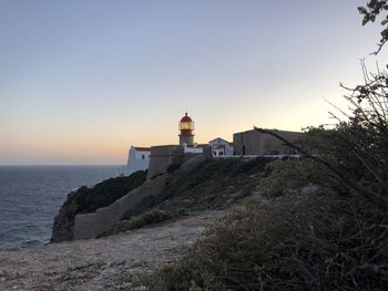 Lighthouse on building by sea against clear sky