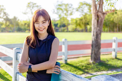 Portrait of smiling young woman standing against trees