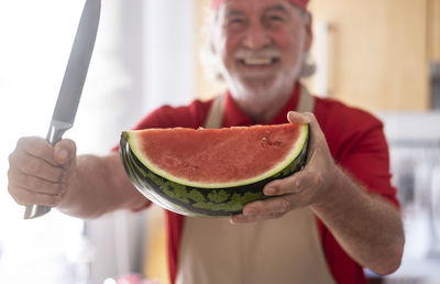 Portrait of senior man holding watermelon at home