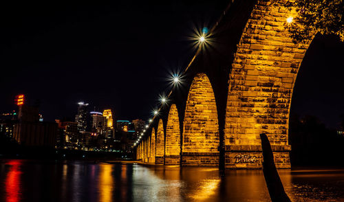 Low angle view of illuminated arch bridge over river at night