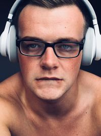 Close-up portrait of shirtless young man listening to music through headphones