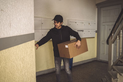 Confident delivery man with package ringing bell for home delivery