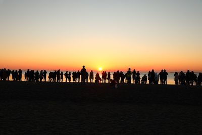 Silhouette people on sand against clear sky during sunset
