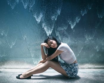 Portrait of young woman sitting against frosted glass