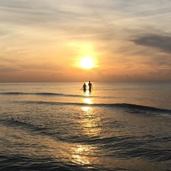 Silhouette people in sea against sky during sunset