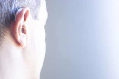 Close-up of man with hearing aid against gray background