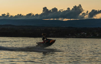 Man sitting on boat in sea against sky during sunset