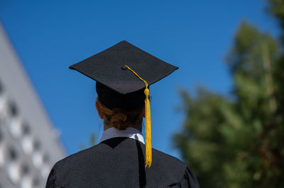 Portrait of woman wearing graduation gown standing against trees