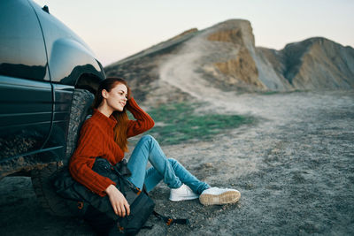 Young woman sitting on rock against mountain