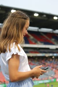 Side view of girl using mobile phone in stadium