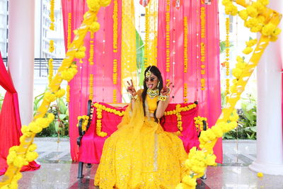 Portrait of bride wearing sunglasses gesturing while sitting on chair at haldi ceremony