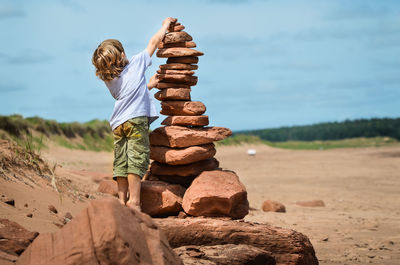 Rear view of boy stacking stones at field