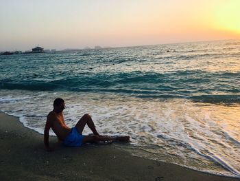 Man sitting on beach against clear sky during sunset