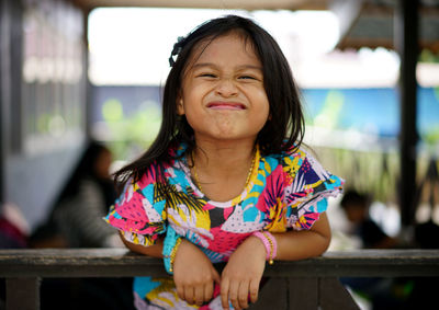 Portrait of playful girl making face while leaning on fence