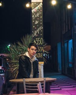 Portrait of young man sitting at sidewalk cafe in city at night