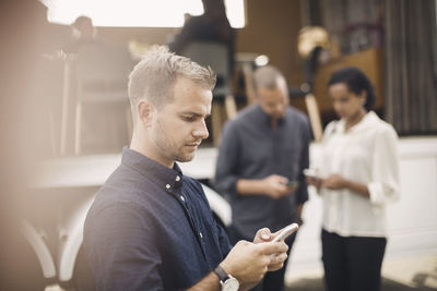 Young businessman using smart phone with colleagues and portable office truck in background