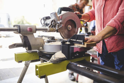 Midsection of senior woman cutting wooden plank with circular saw at workshop