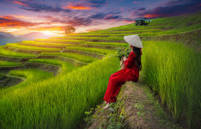 Side view of woman sitting on field against sky