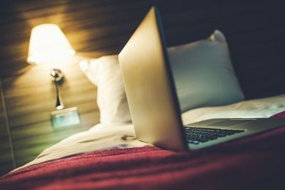 Close-up of laptop on bed in illuminated bedroom