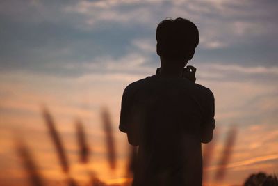 Rear view silhouette of man standing against sky during sunset