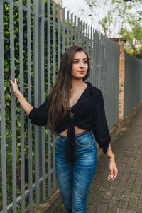 Portrait of beautiful young woman standing against fence