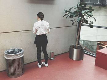 Full length rear view of woman standing by garbage bin at university