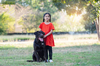 A lovely southeast asian child girl in red outfits plays with her big dog in the back or front yard