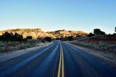 Road passing through land against clear blue sky