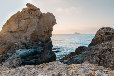 Rock formation on beach against sky during sunset