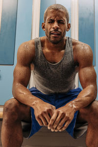 Tired male athlete with eyes closed sitting on bench in locker room