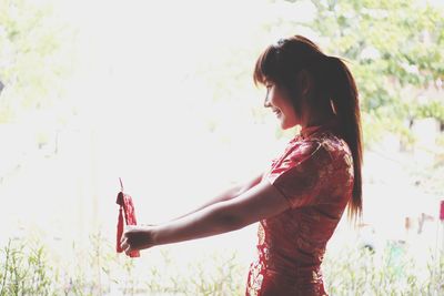 Side view of young woman standing against plants