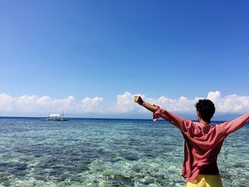 Rear view of man standing by sea against blue sky
