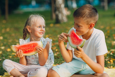 Happy kids eating watermelon sitting at park