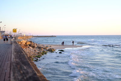 People on beach against clear sky during sunset