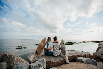 People sitting on rock by sea against sky
