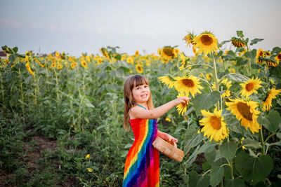 Portrait of smiling woman with sunflower in field against sky