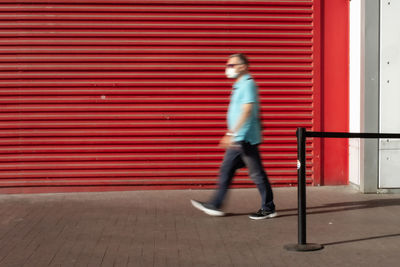 Side view of man walking against red wall