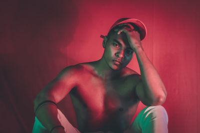 Portrait of young man sitting against red background