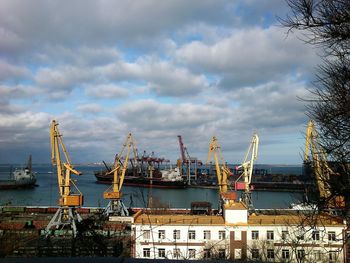 Cranes at harbor against sky in city