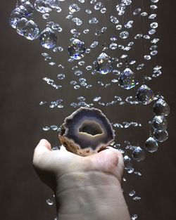 Cropped image of hand holding stone by crystals against brown background