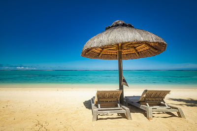 Deck chairs on sand at beach against clear blue sky