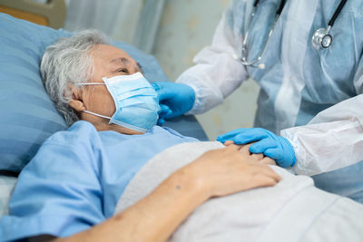 Midsection of doctor consoling patient wearing flu mask at hospital
