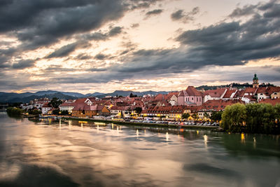 Townscape by river against sky during sunset