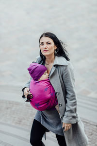 Woman carrying son in scarf on steps